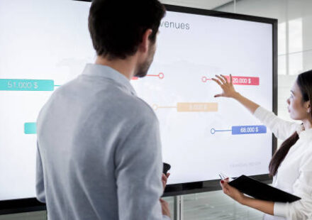 A lady using a touchscreen in an office to demonstrate to a man
