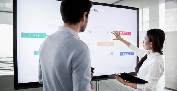 A lady using a touchscreen in an office to demonstrate to a man
