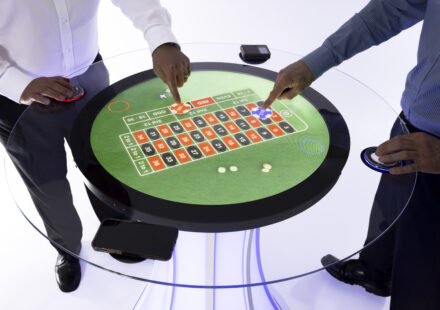 A round touchscreen table with 2 people playing roulette